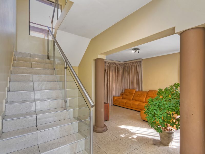 Open plan living area featuring a tiled staircase with a modern glass and stainless steel balustrade and structural columns.