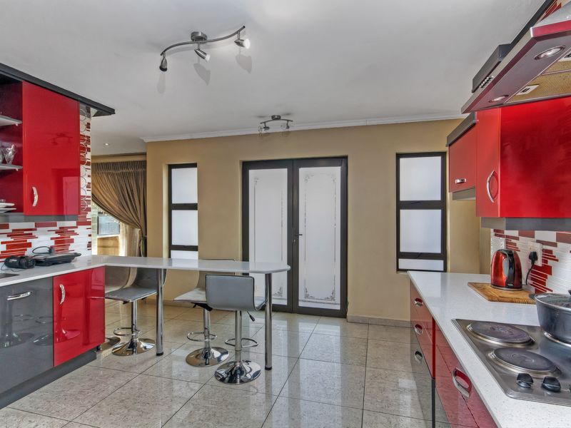 Modern kitchen featuring high-gloss red cabinetry, stone countertops, integrated hob with extractor, and tiled flooring with direct access to the outdoor area.