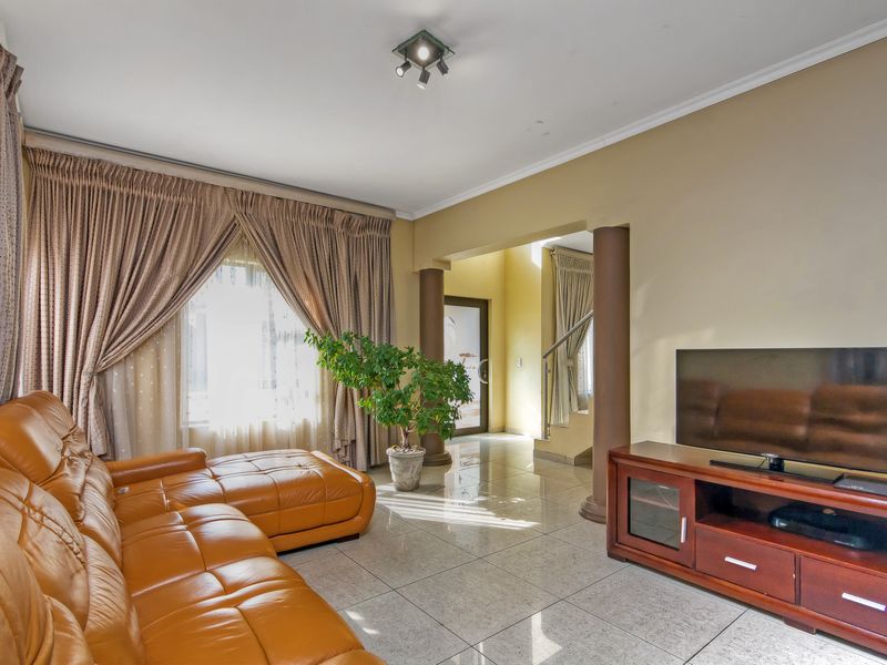 Spacious living room featuring polished tiled flooring, decorative structural columns, and access to the hallway and staircase area.