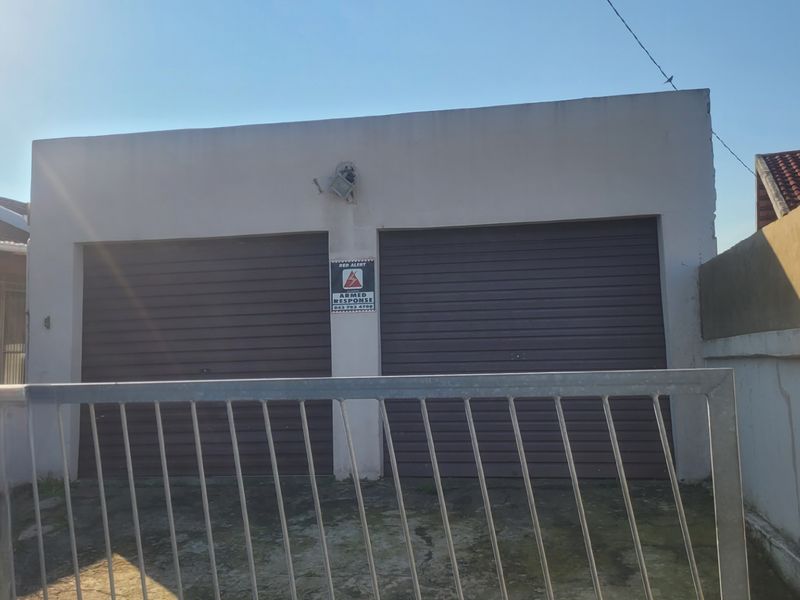A double garage with roller doors, secured by a metal gate and perimeter walling, featuring an exterior security light.