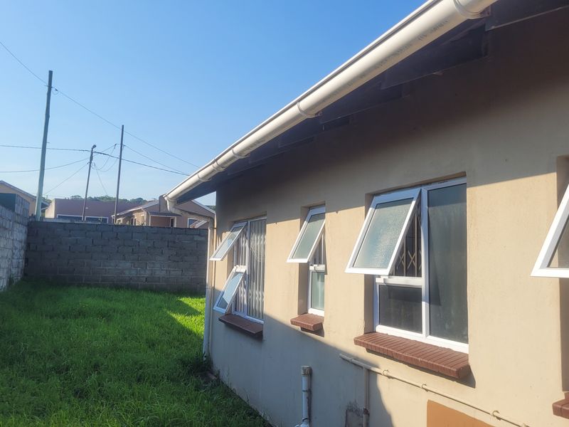 Rear exterior view of the property showing the back wall, casement windows with security bars, guttering, and a surrounding brick boundary wall.