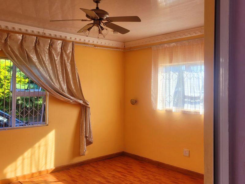 A bright, empty bedroom featuring laminate flooring, a ceiling fan, and security bars on the windows.