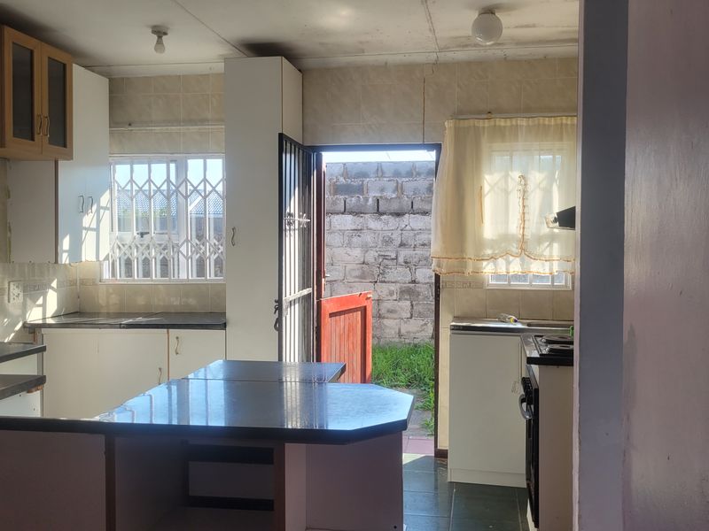 Functional kitchen featuring built-in cabinetry, laminate countertops, and direct access to the rear exterior, offering potential for modernization and cosmetic updates.