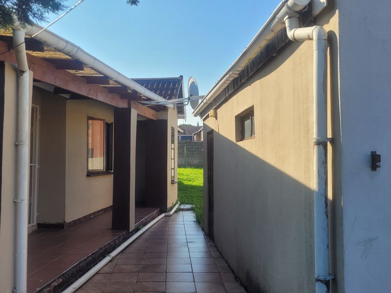 A paved exterior walkway between the main house structure and a garage, featuring a covered patio area and functional rainwater drainage systems.