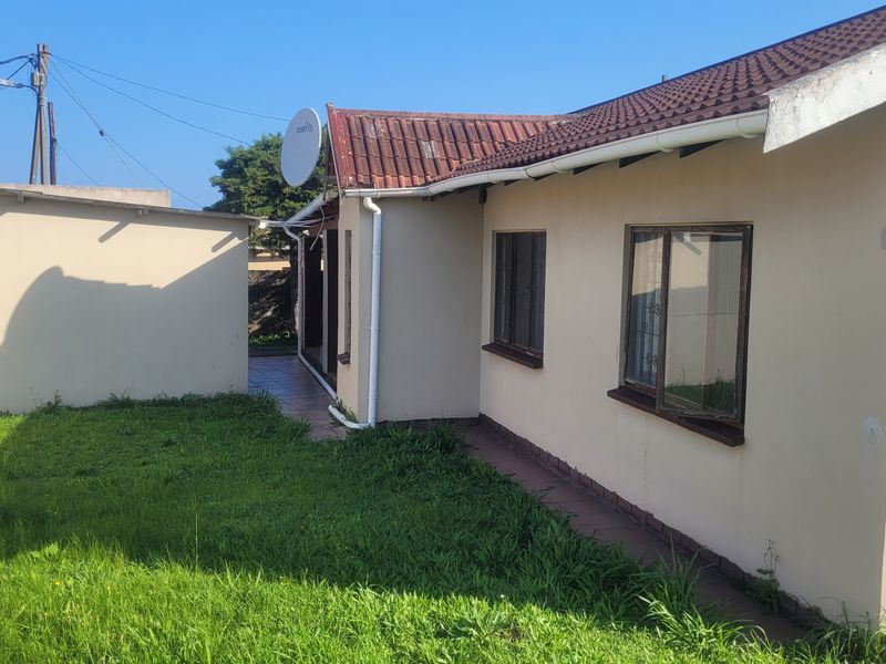 Rear view of the house showing the exterior wall, tiled roof, and surrounding garden area.
