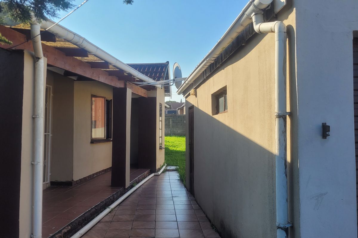 A paved exterior walkway between the main house structure and a garage, featuring a covered patio area and functional rainwater drainage systems.