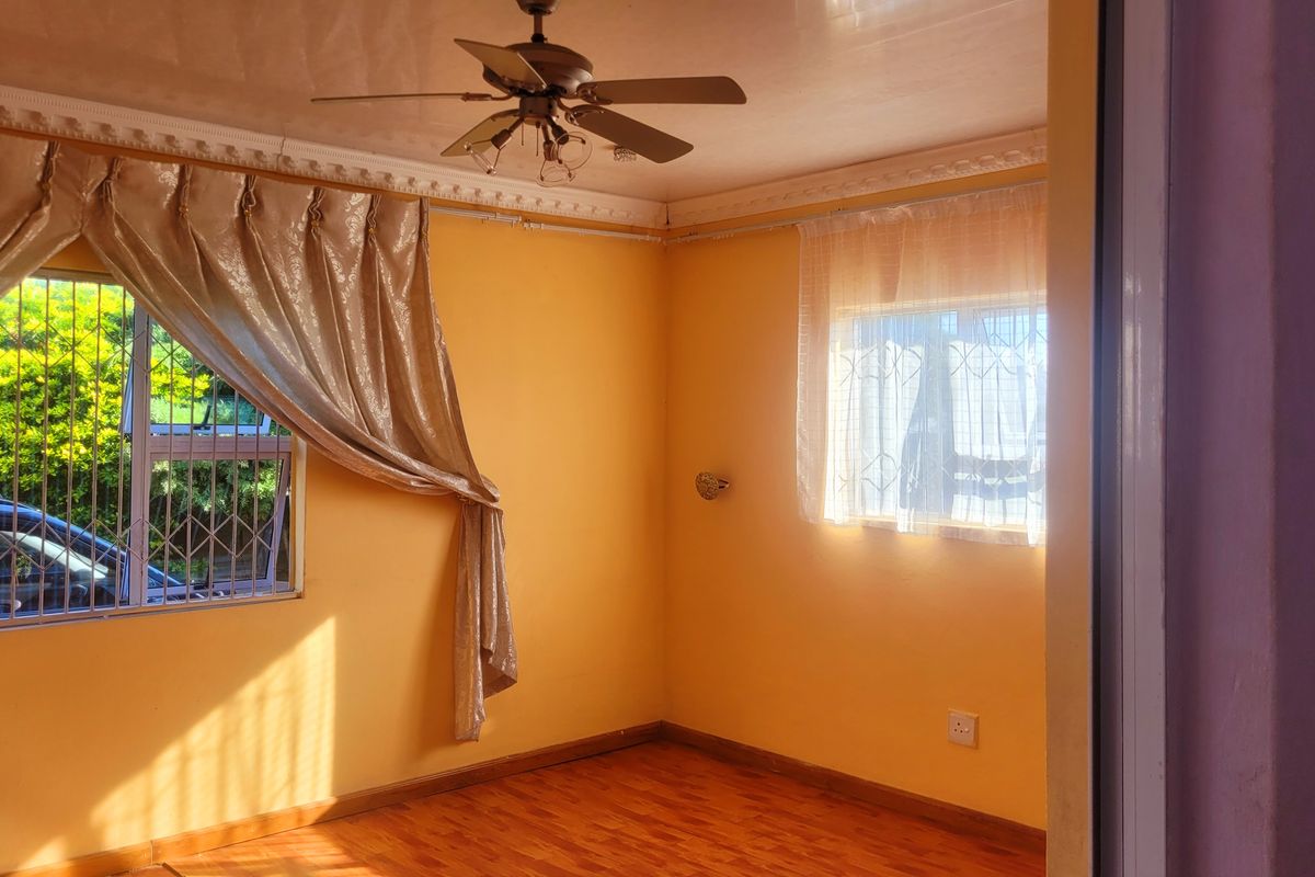 A bright, empty bedroom featuring laminate flooring, a ceiling fan, and security bars on the windows.