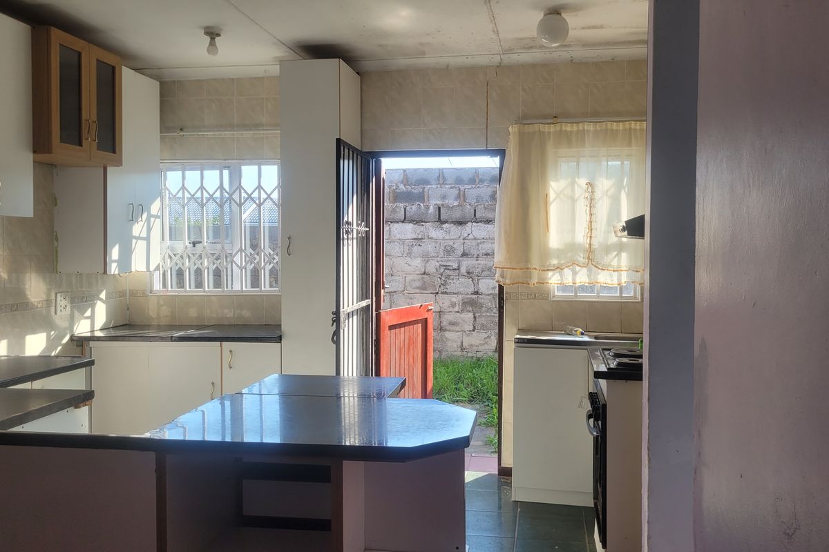 Functional kitchen featuring built-in cabinetry, laminate countertops, and direct access to the rear exterior, offering potential for modernization and cosmetic updates.