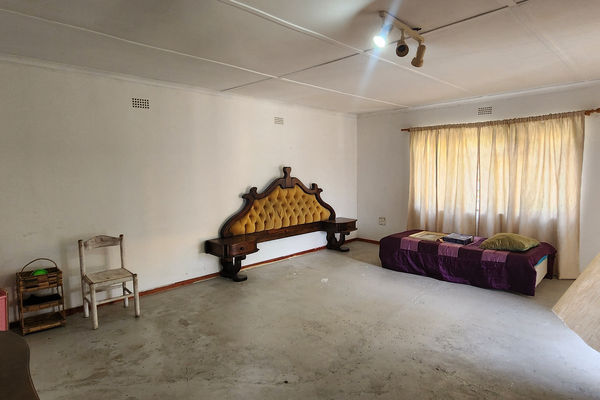Spacious bedroom featuring a large built-in headboard, concrete flooring, and natural light through window curtains.