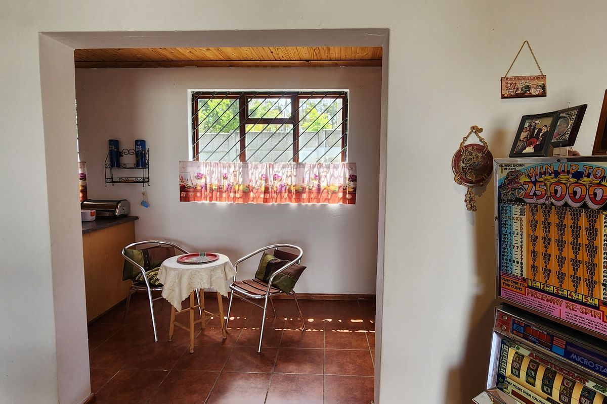 A view through a doorway into a kitchen area featuring tiled flooring, a timber ceiling, and a window with security bars.