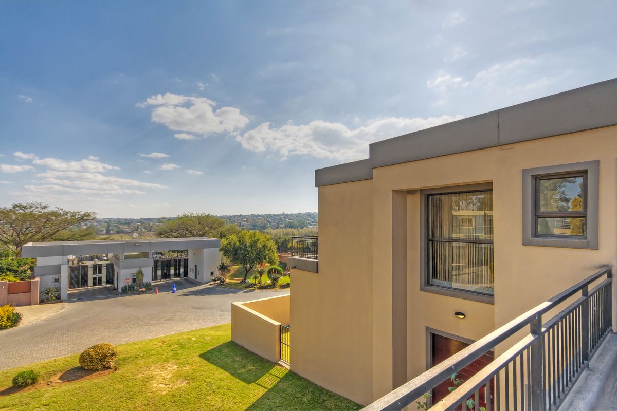 Elevated view of the property exterior, showcasing the modern facade, balcony railing, and the surrounding estate entrance and landscape.