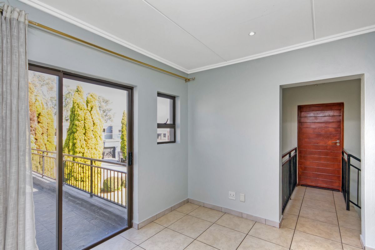 A bright, empty room featuring tiled flooring, a sliding glass door leading to a balcony, and access to a hallway with a wooden door.