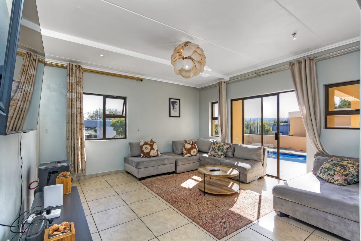 Bright living room featuring tiled flooring, large windows, and sliding glass doors providing direct access to the outdoor pool area.