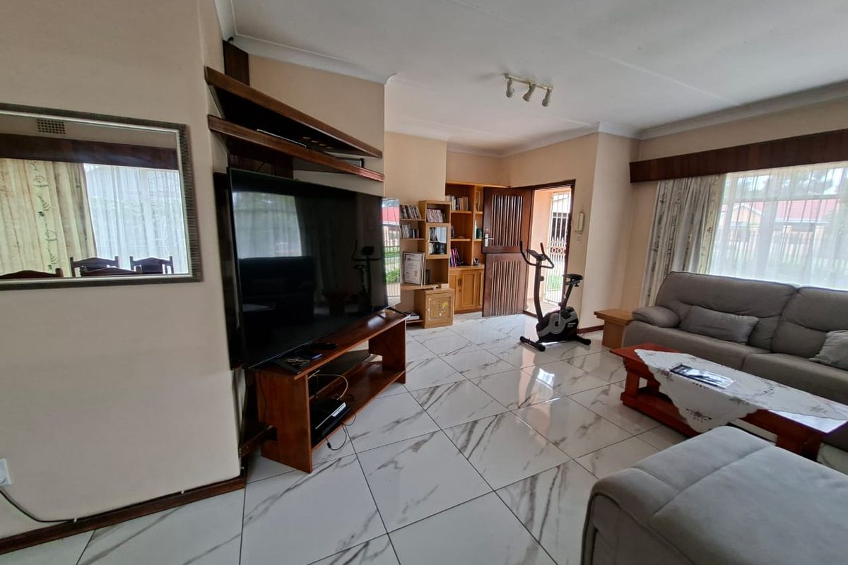 Spacious living room featuring modern marble-look floor tiles, built-in wooden shelving, and direct access to the exterior through a security gate.