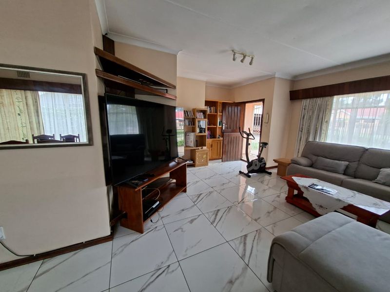 Spacious living room featuring modern marble-look floor tiles, built-in wooden shelving, and direct access to the exterior through a security gate.