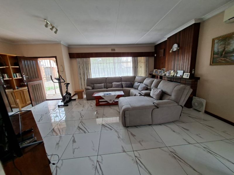 Spacious living room featuring large marble-look floor tiles, a wood-paneled feature wall with a brick fireplace, and built-in shelving.