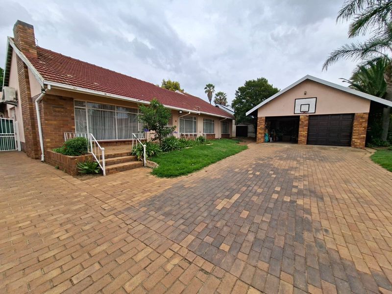 Front exterior view of a brick house featuring a paved driveway, raised patio entrance, and a detached double garage.