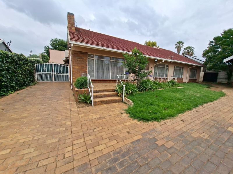 Front exterior view of a single-story brick house featuring a paved driveway, tiled roof, and a small elevated entrance porch with metal railings.