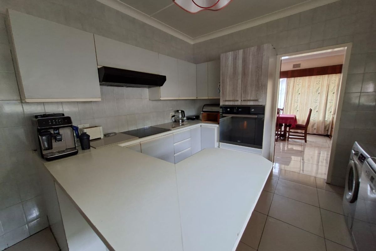 A functional kitchen featuring built-in cabinetry, an integrated oven, a ceramic hob, and tiled finishes, with an open flow into the adjacent dining area.