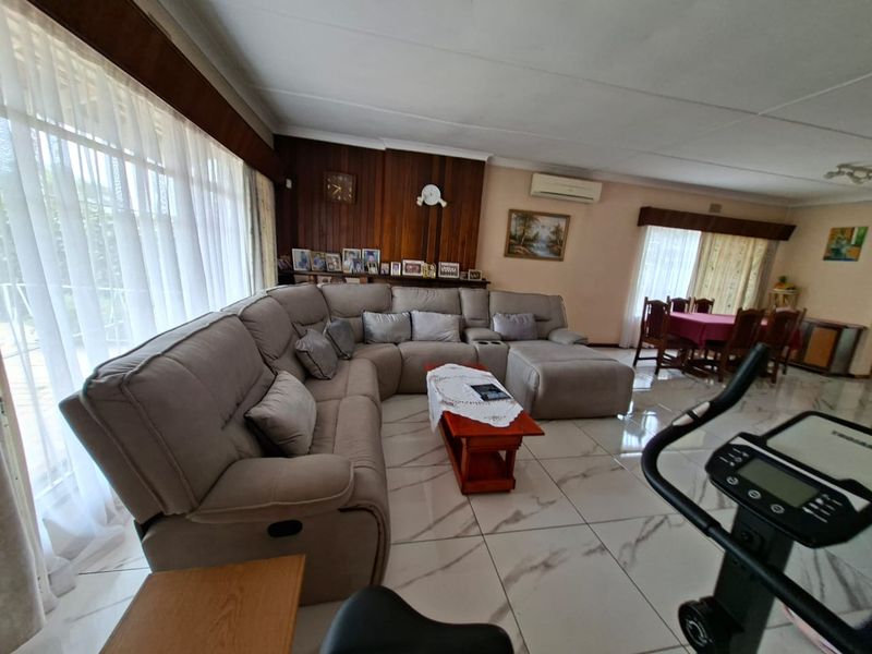 Spacious open-plan living and dining area featuring large format tiled flooring, wood-paneled feature wall, and split system air conditioning.