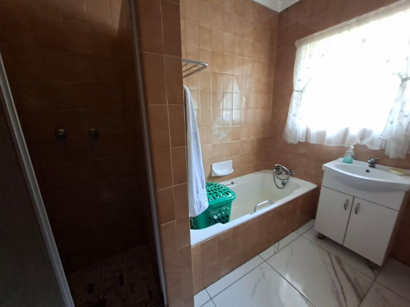 A functional bathroom featuring a built-in bathtub, separate shower enclosure, and a vanity unit with tiled walls and flooring.