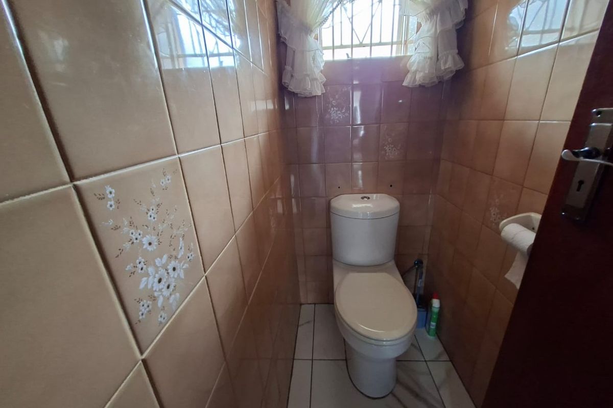 A compact guest bathroom featuring dated ceramic wall tiles, a standard toilet, and a small window with security bars.