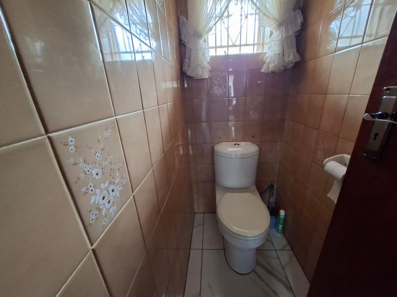 A compact guest bathroom featuring dated ceramic wall tiles, a standard toilet, and a small window with security bars.