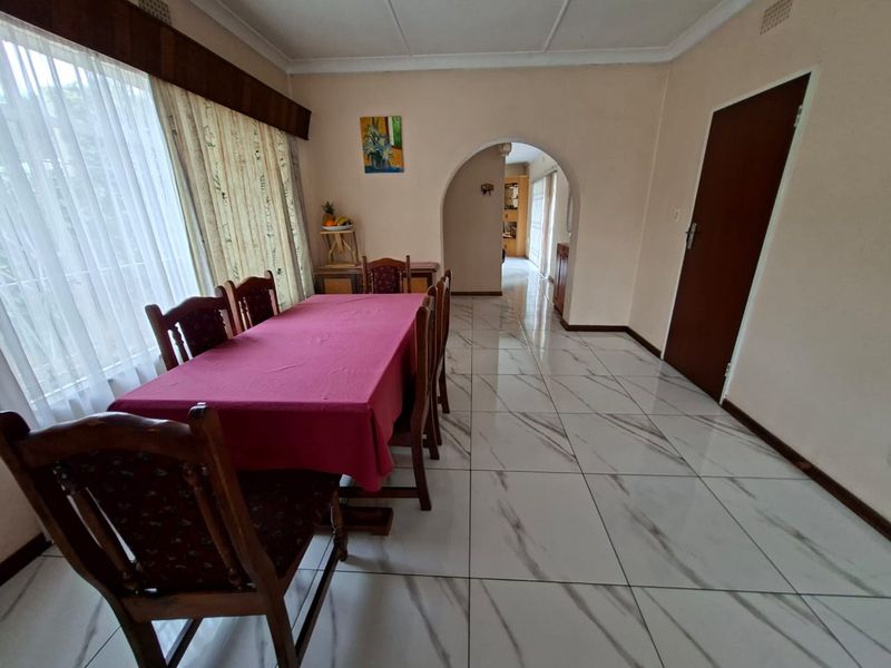 A dining room featuring large format marble-look floor tiles, a decorative archway leading to the hallway, and classic ceiling cornicing.