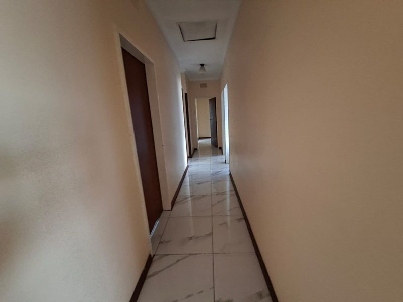 A long, empty hallway featuring white marble-look floor tiles and multiple doorways leading to other rooms in the house.