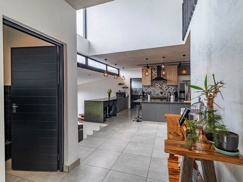 Modern open-plan kitchen and living area featuring double volume ceilings, sleek cabinetry, a central island, and contemporary tiled flooring with abundant natural light.