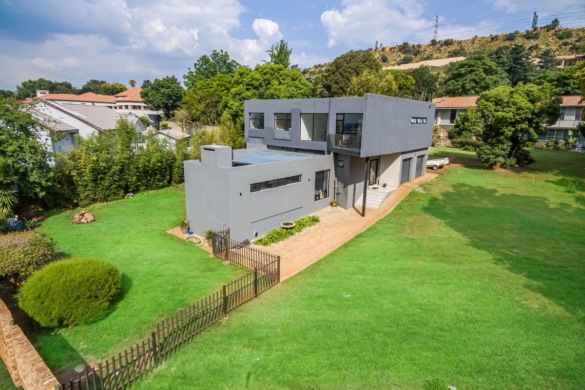Aerial view of a modern two-story grey house featuring a spacious lawn, metal fencing, and a balcony, set within a residential neighborhood.