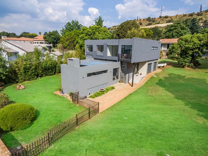 Aerial view of a modern two-story grey house featuring a spacious lawn, metal fencing, and a balcony, set within a residential neighborhood.