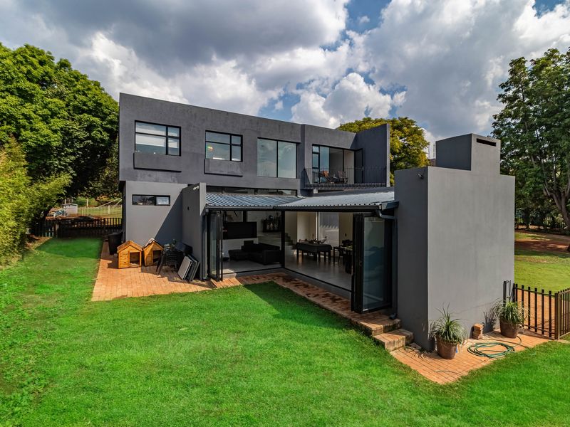 Rear view of a modern two-story house featuring a covered patio with bi-fold doors, a balcony, and a spacious landscaped garden.