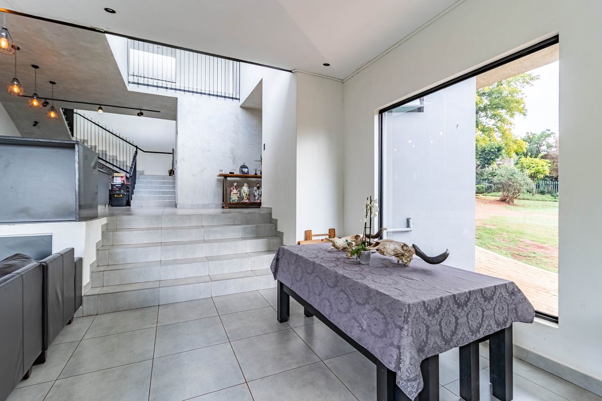 Spacious living area featuring modern tiled flooring, a prominent staircase with metal balustrades, and a large window providing views of the garden.