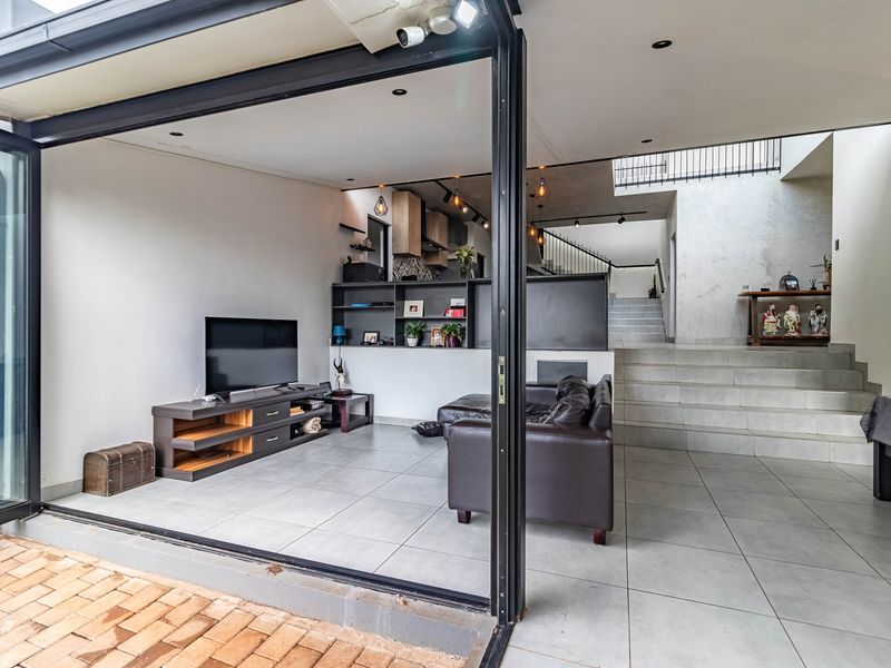 Modern open-plan living area featuring large format floor tiles, built-in shelving, and seamless indoor-outdoor flow through expansive sliding glass doors.