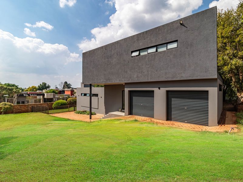 Modern double-story home featuring a dark grey facade, double roller shutter garage doors, and a spacious front lawn.