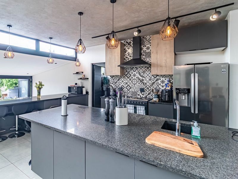 Modern open-plan kitchen featuring a large island with granite countertops, patterned tile backsplash, sleek cabinetry, and contemporary pendant lighting in a bright, airy space.