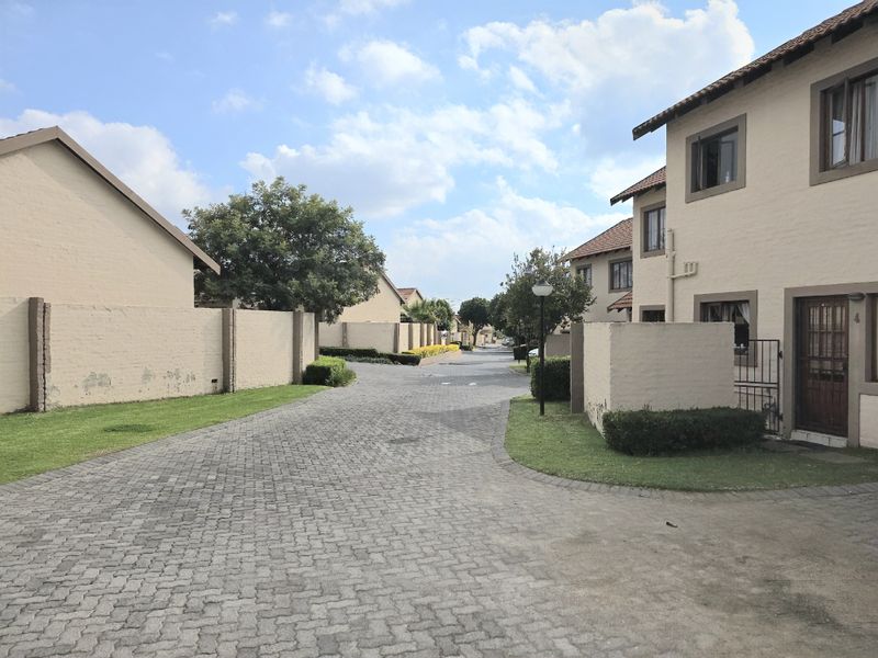 A view of the complex street showing paved driveways, boundary walls, and townhouse facades with tiled roofs.