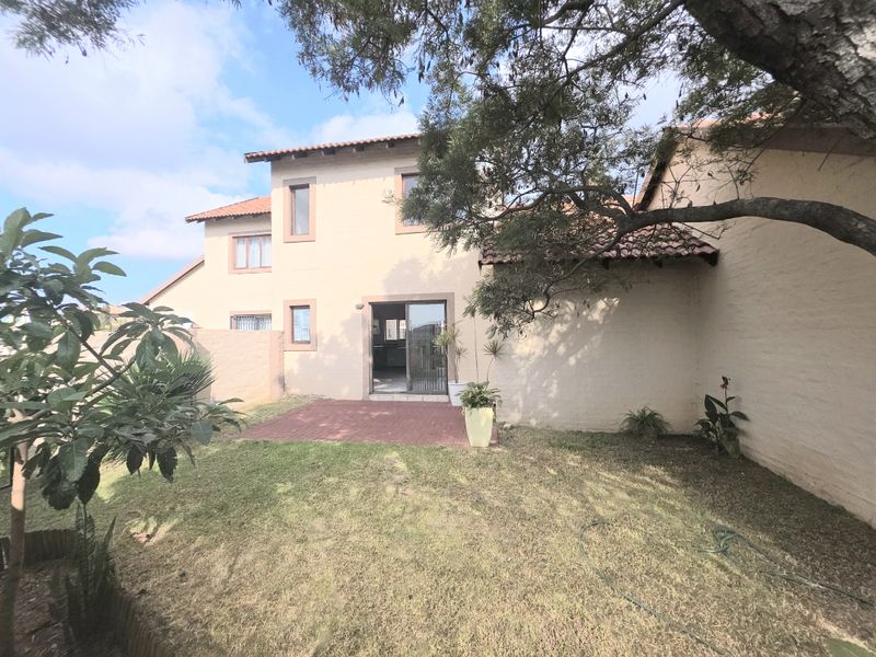 Rear view of the townhouse featuring a private garden, brick paved patio area, and sliding glass door access to the interior living space.
