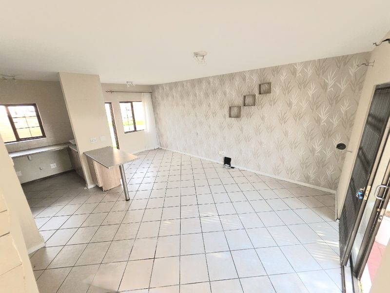 An open-plan living and kitchen area featuring tiled flooring, a breakfast bar, and decorative wallpaper, offering a versatile space for modern living.