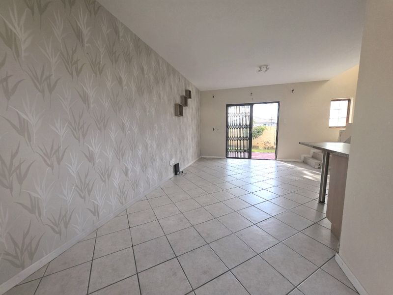 An open-plan living area featuring tiled flooring, a breakfast bar, and a sliding door leading to the exterior, providing a blank canvas for customization.