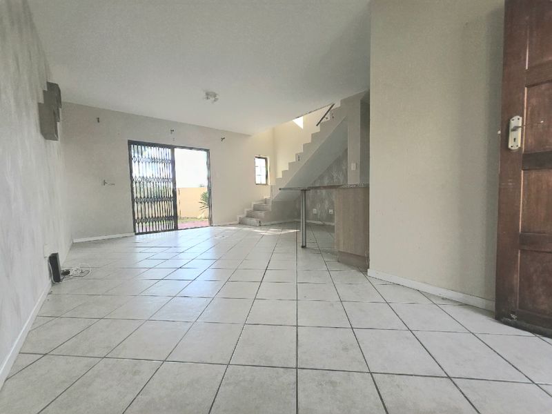 An open-plan living area featuring tiled flooring, a breakfast bar, and a staircase leading to the upper level, with access to the exterior.