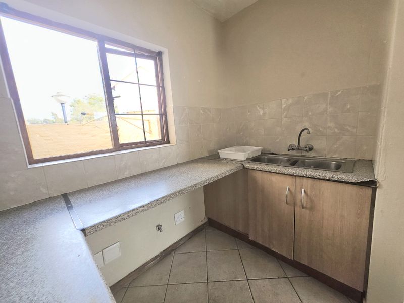 A functional kitchen area featuring laminate countertops, a double bowl stainless steel sink, tiled splashback, and base cabinetry with tiled flooring.