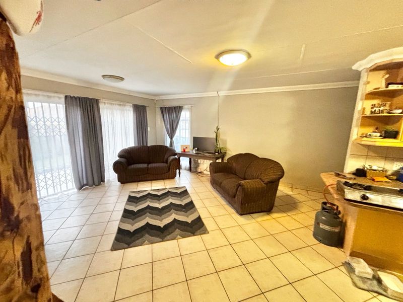 Open plan living area featuring tiled flooring, sliding doors with security gates, and an integrated kitchen space with cabinetry.