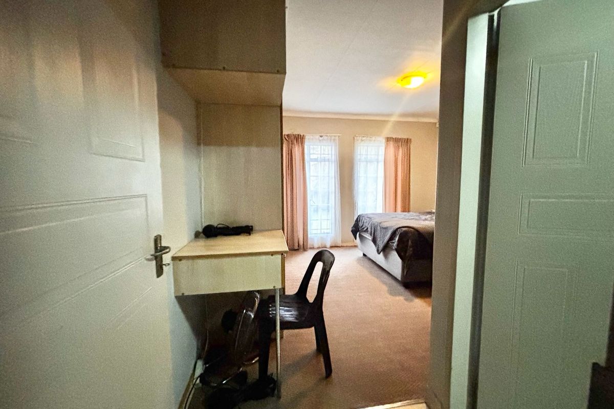 A bedroom featuring carpeted flooring and a built-in desk with overhead shelving, viewed from an adjacent hallway.