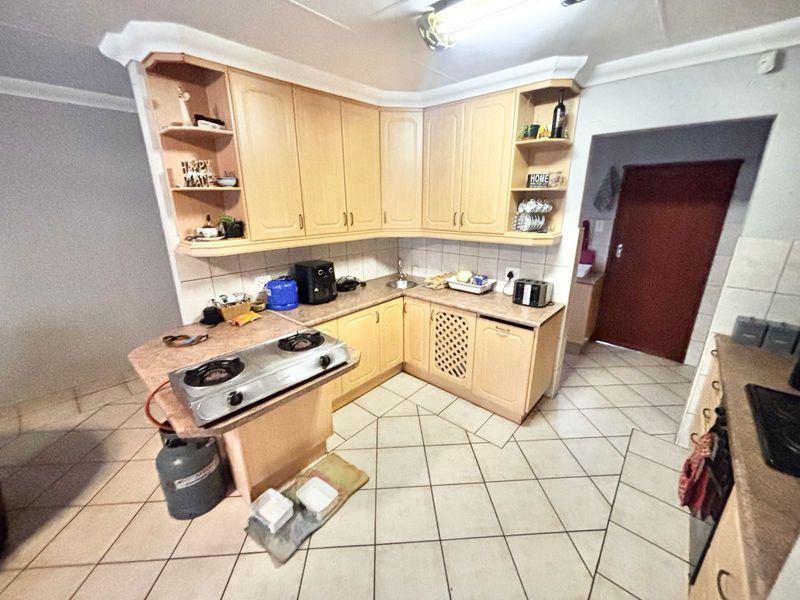 A functional kitchen featuring light wood-tone cabinetry, tiled splashbacks, and tiled flooring, offering a practical layout with integrated storage and workspace.