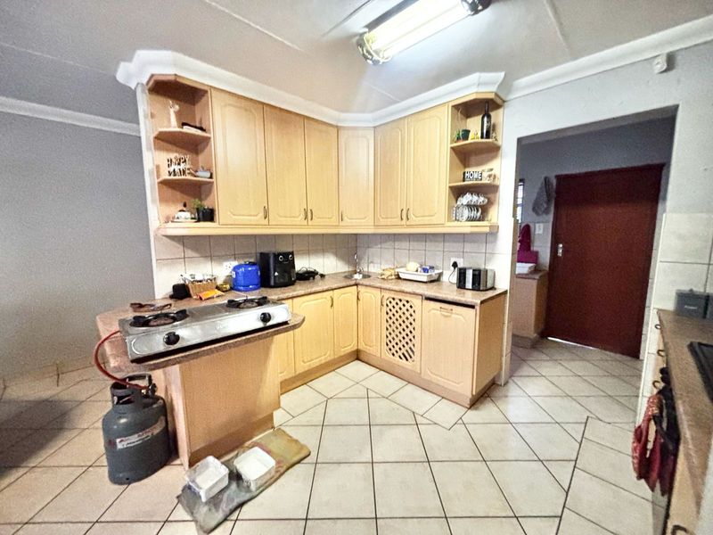 A functional kitchen featuring light wood-tone cabinetry, tiled flooring, and a tiled backsplash, offering a practical layout with ample storage space.