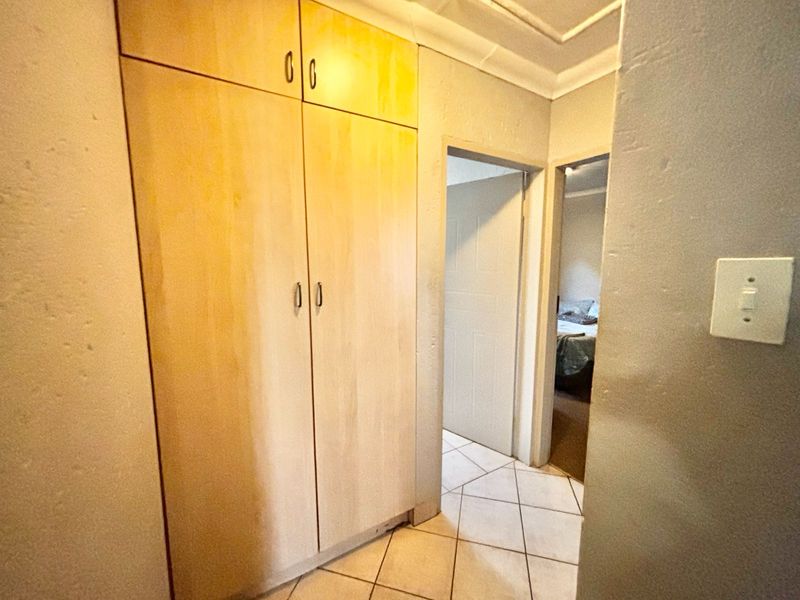 A functional hallway featuring built-in wooden cupboards, tiled flooring, and coved ceiling details, providing access to adjacent rooms.