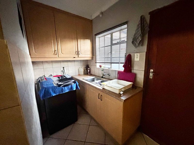 A functional scullery area featuring built-in wooden cabinetry, a stainless steel sink, tiled splashbacks, and tiled flooring.