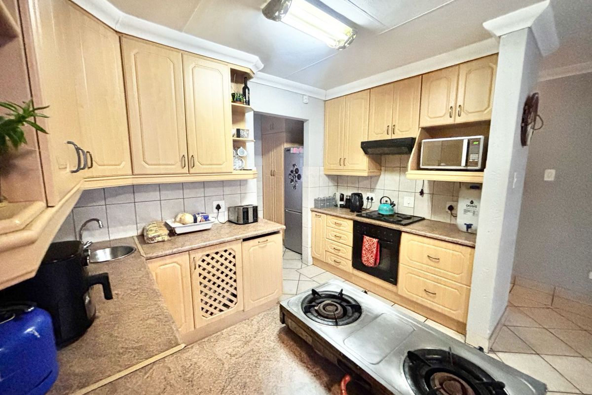 A functional kitchen featuring light wood-tone cabinetry, laminate countertops, built-in oven, hob, and extractor fan with tiled backsplash and flooring.